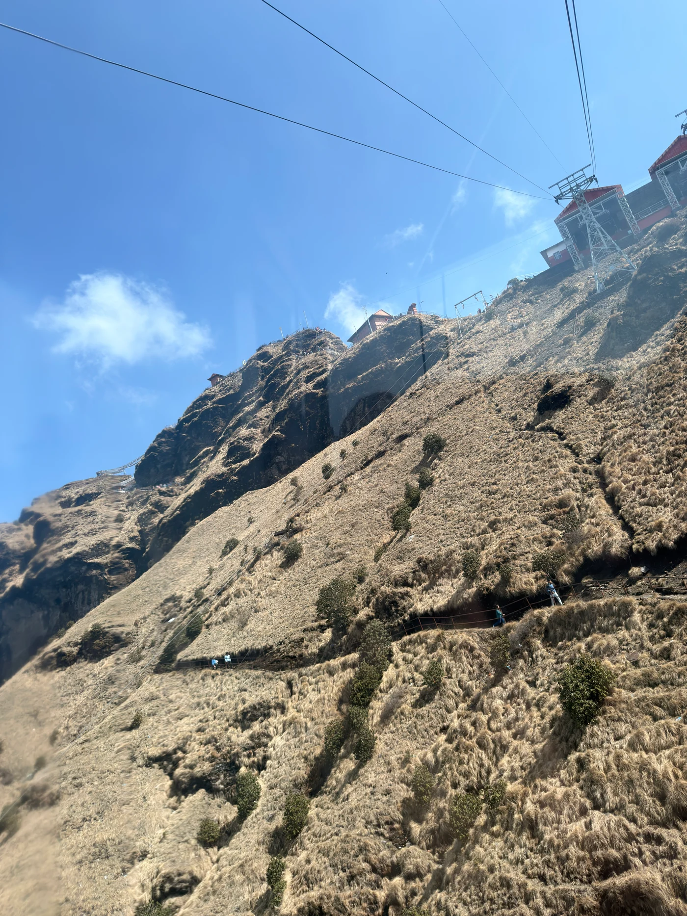 Cable car wires stretching up a steep grassy slope beneath a bright blue sky