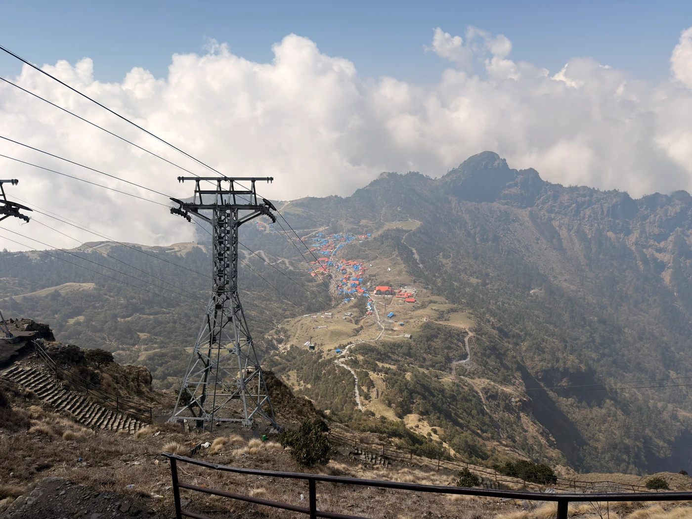 Cable car lines crossing a mountain valley above a village with red and blue roofs