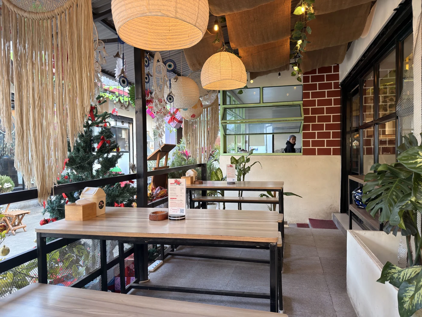 Wooden café tables beneath warm paper lanterns, with hanging woven decorations and green plants