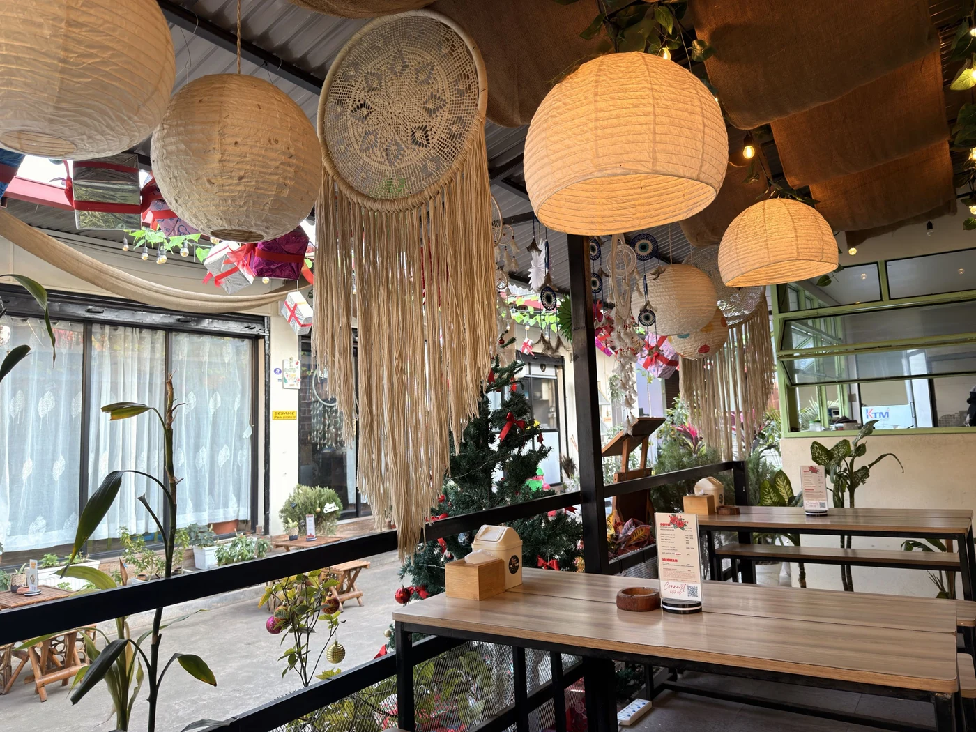 Glowing paper lanterns and long woven decorations above a café seating area