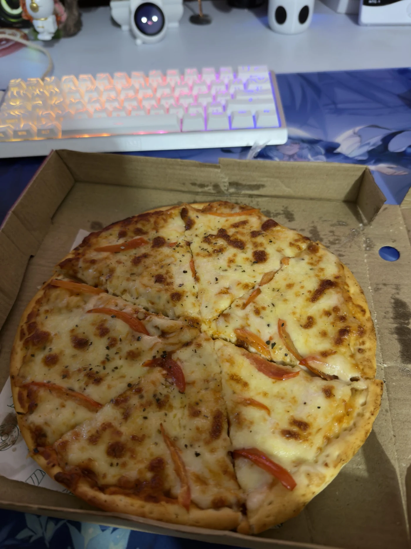 A pizza in an open box beside a glowing keyboard
