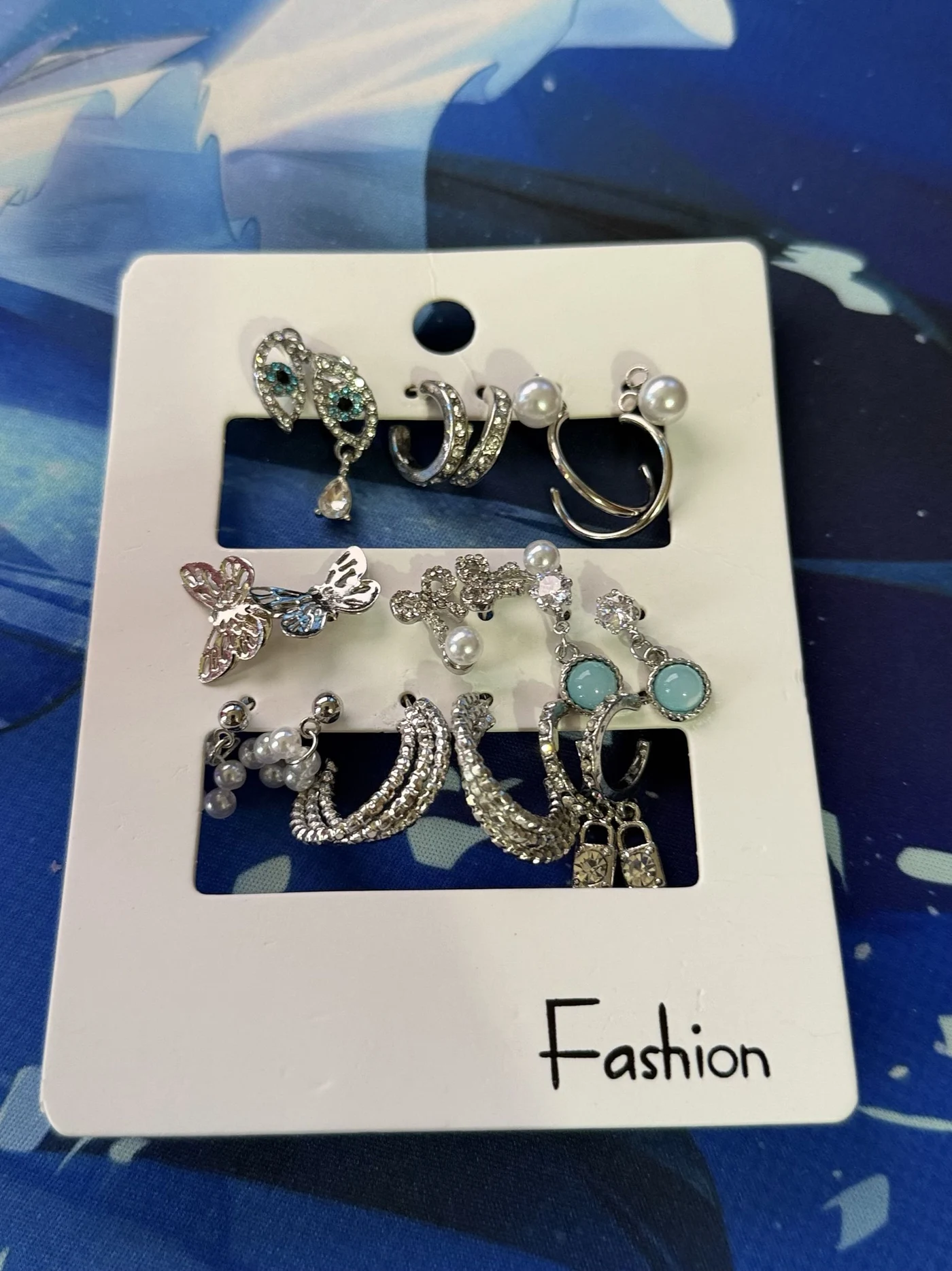 Silver-toned earrings with pearls, butterflies, and pale blue stones on a display card