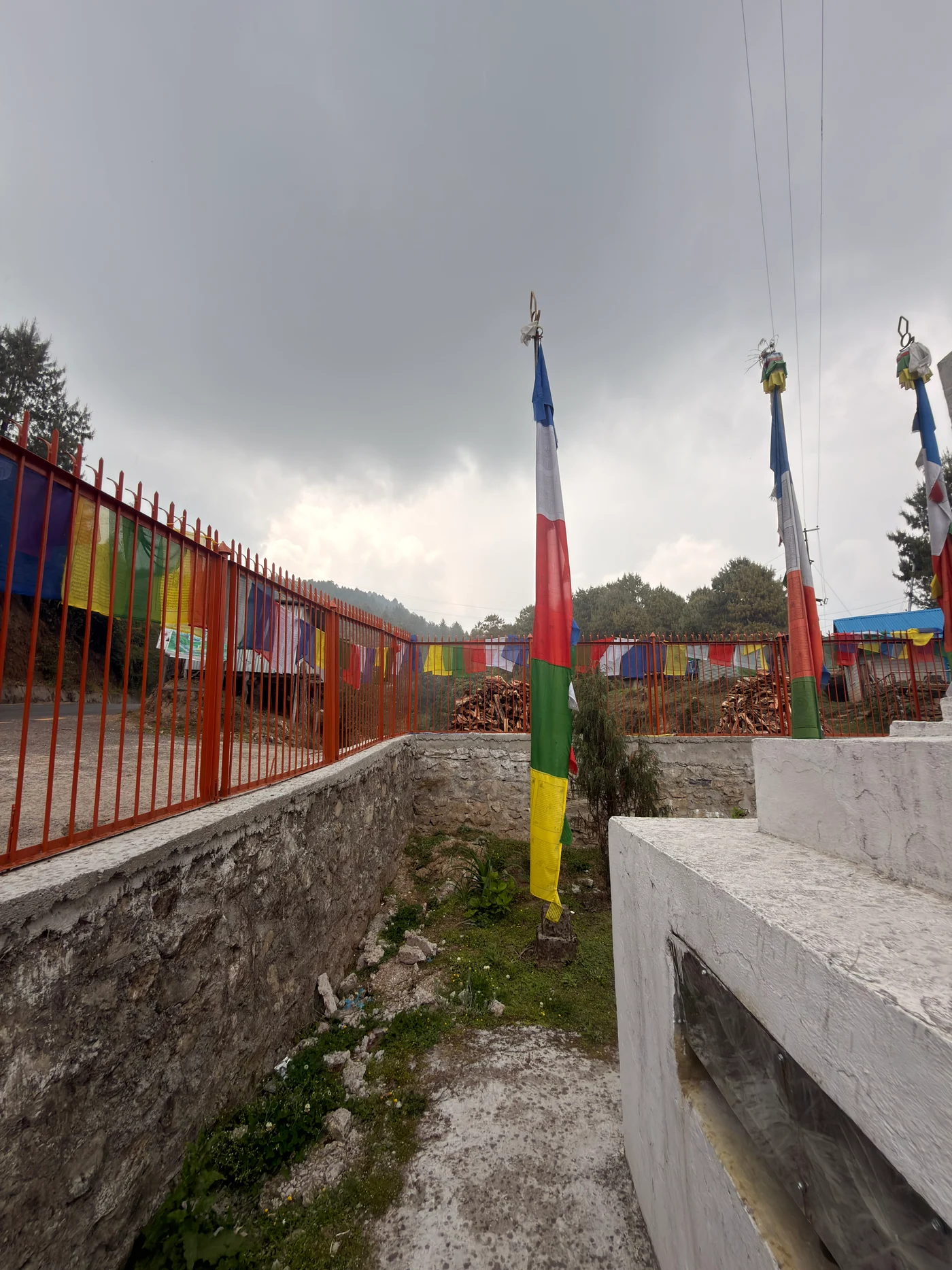 Tall multicoloured prayer flags beside a red fence beneath an overcast sky