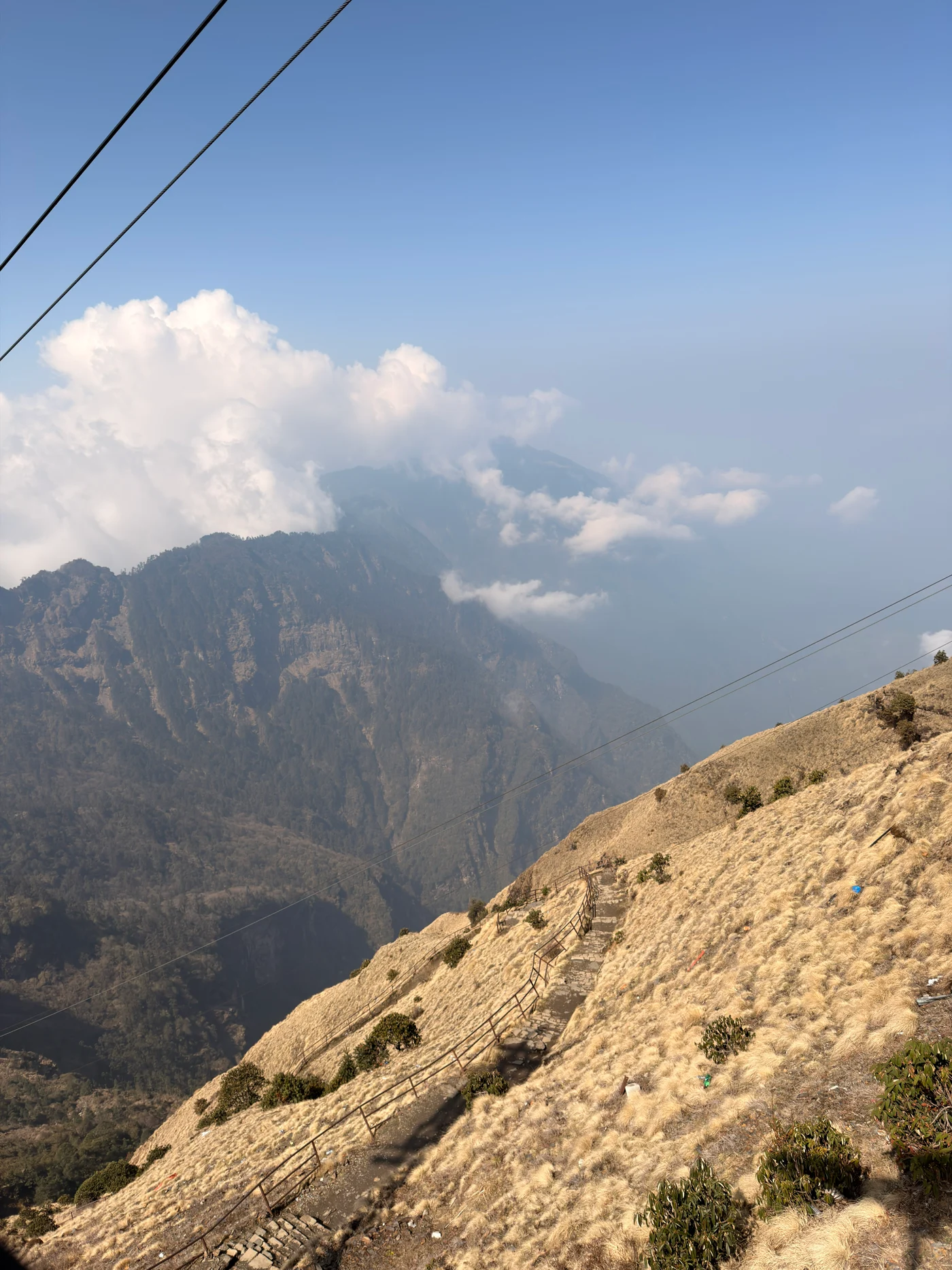 A narrow staircase winding across a golden hillside below cloud-covered mountains