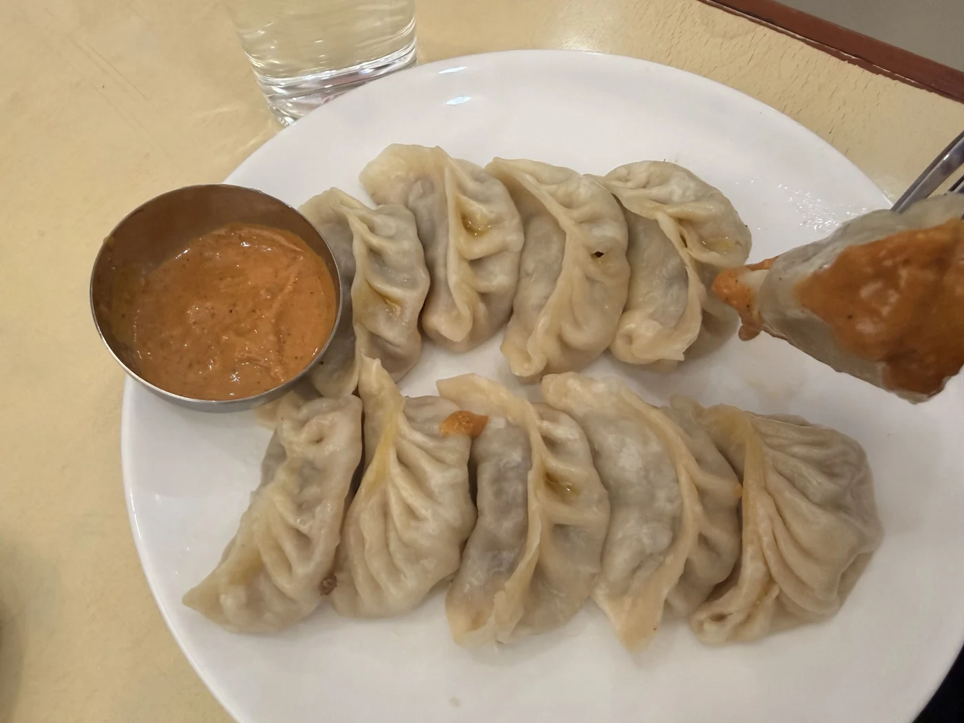 Pleated steamed dumplings with a bowl of orange dipping sauce