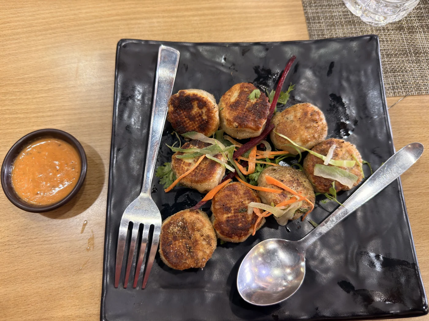 Golden pan-fried rounds on a black plate beside dipping sauce