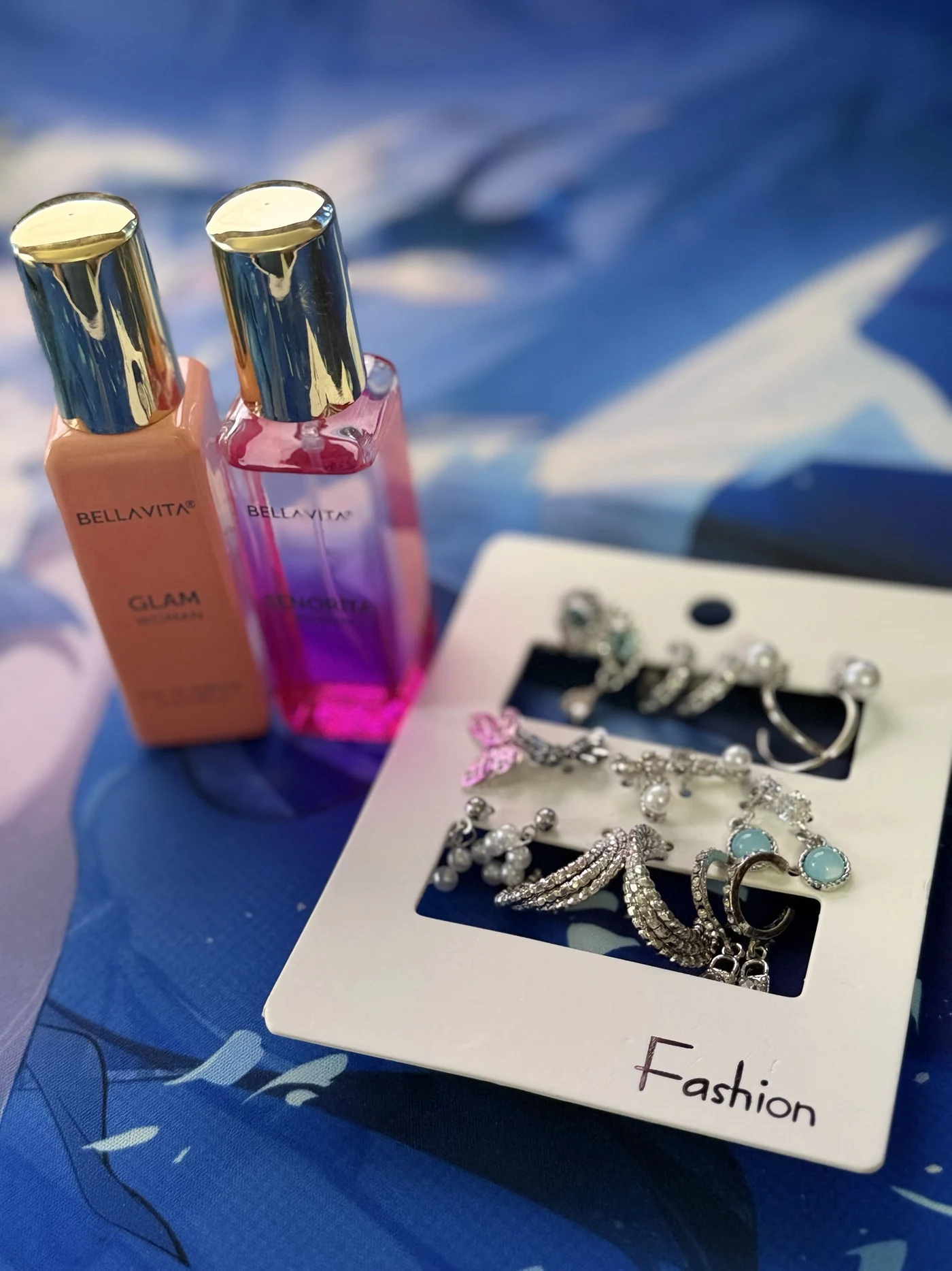 Two perfume bottles beside a card of earrings on blue illustrated fabric