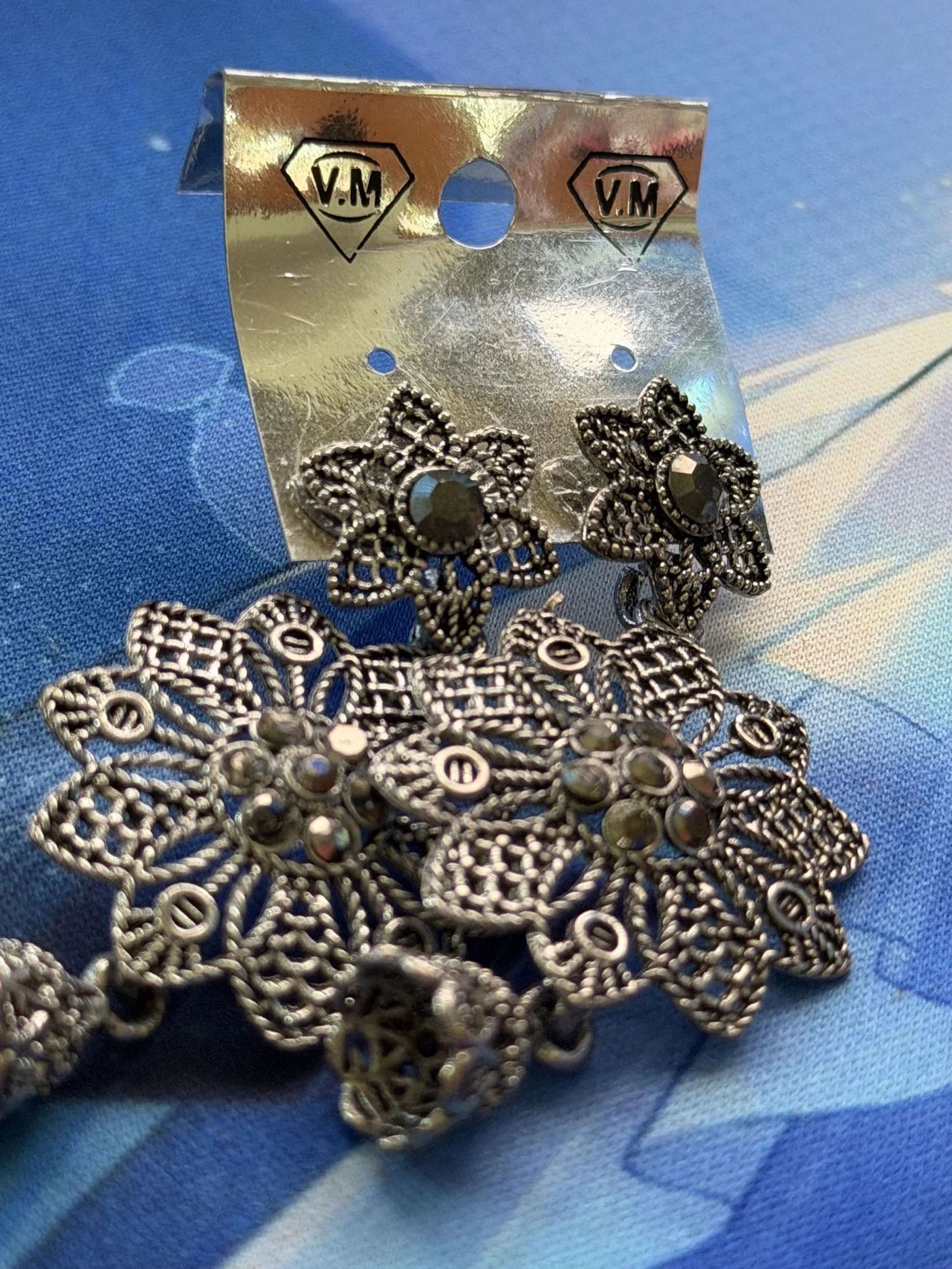 An ornate pair of silver-toned floral earrings on blue fabric