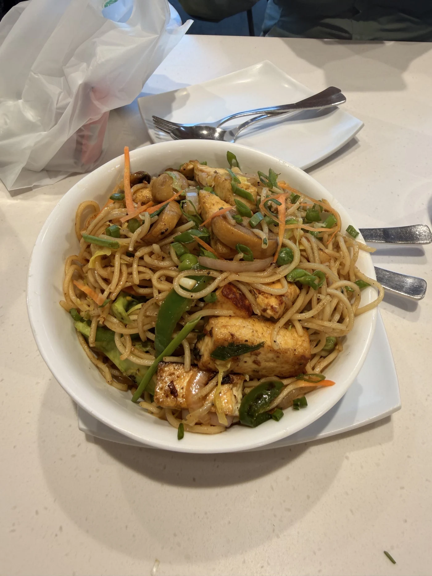 Noodles with vegetables, mushrooms, and golden pieces in a white bowl