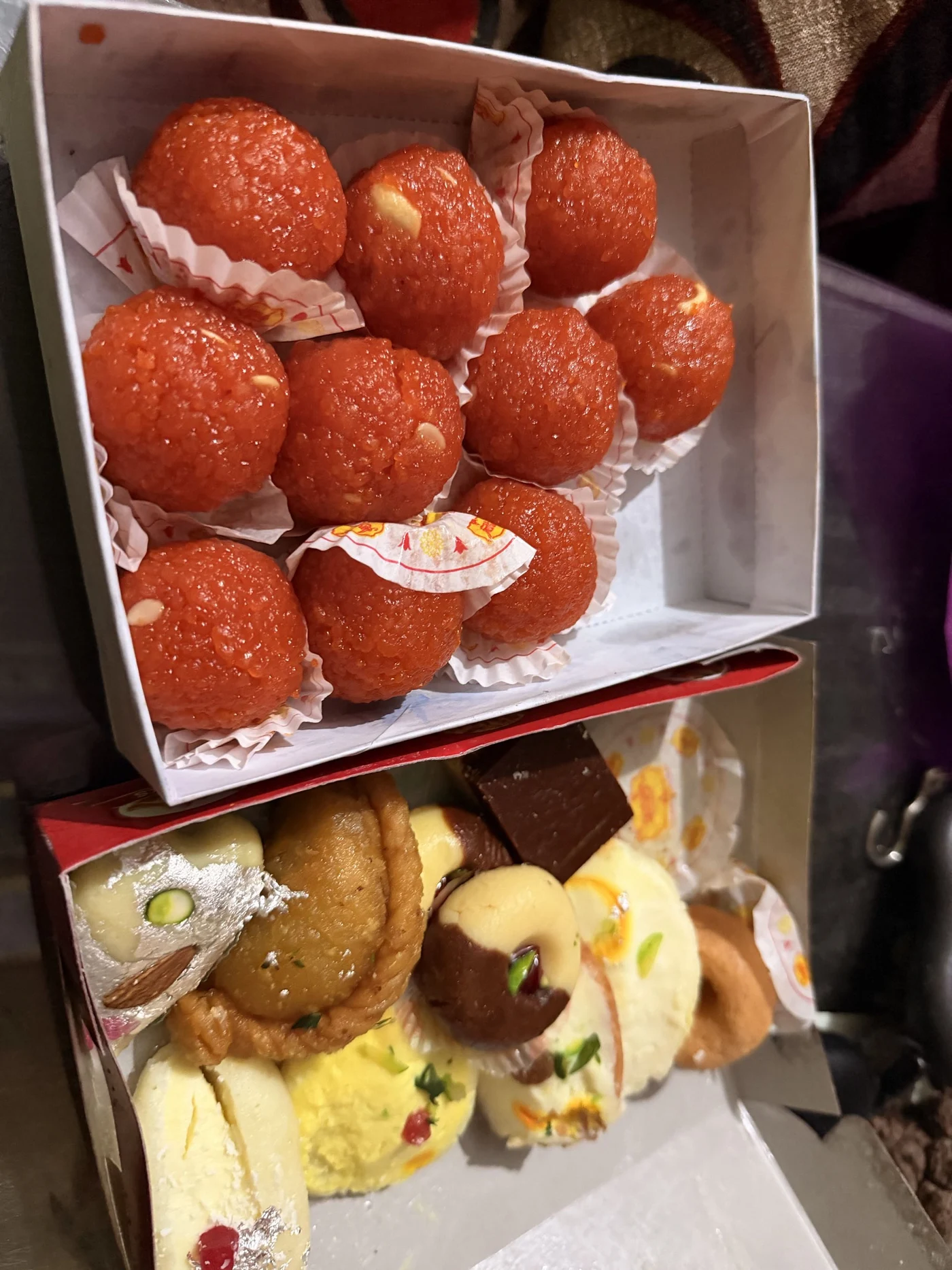 Open boxes of orange round sweets and assorted decorated sweets viewed at an angle