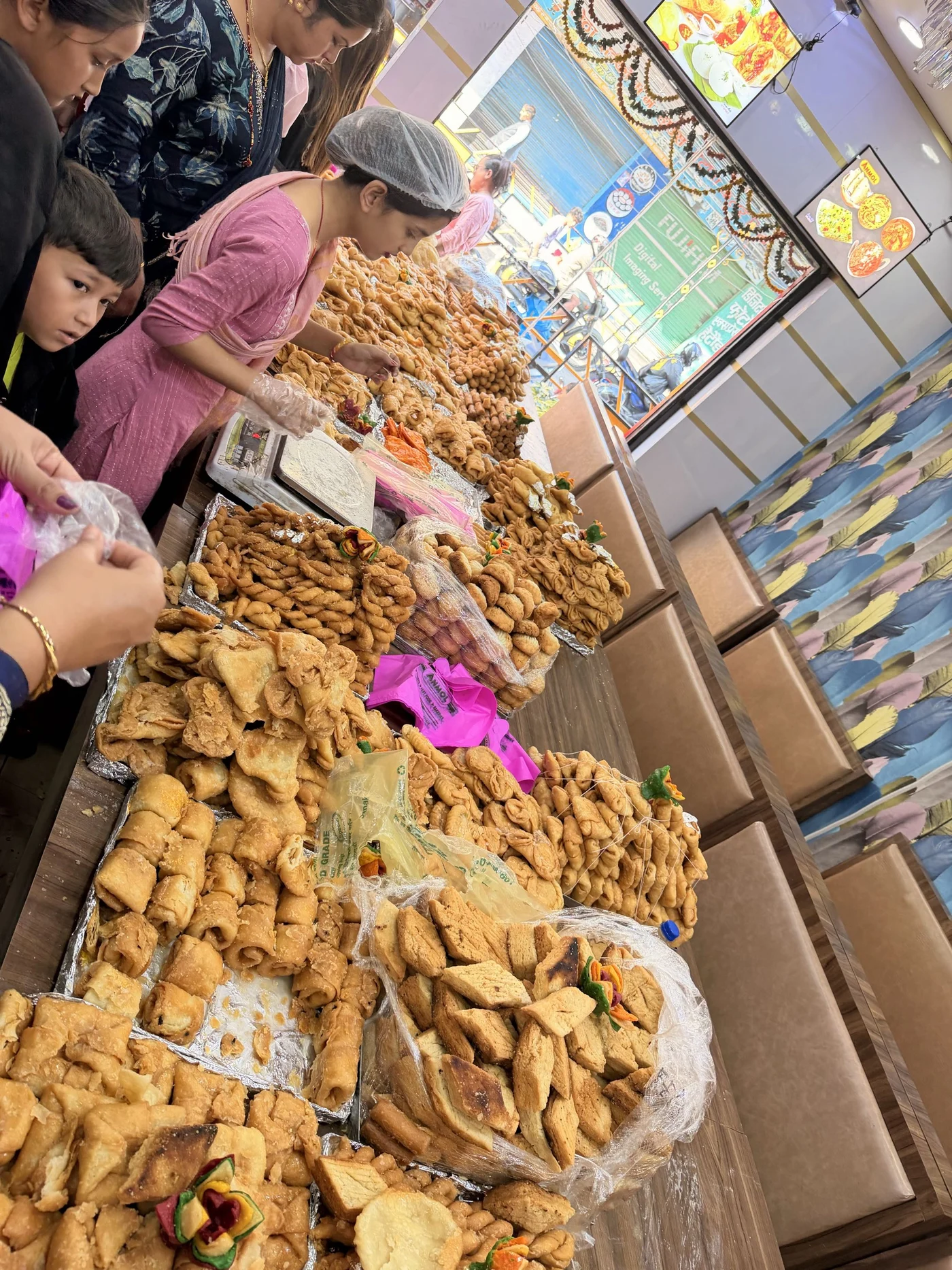 A busy sweet shop counter with trays of pastries and a person serving customers