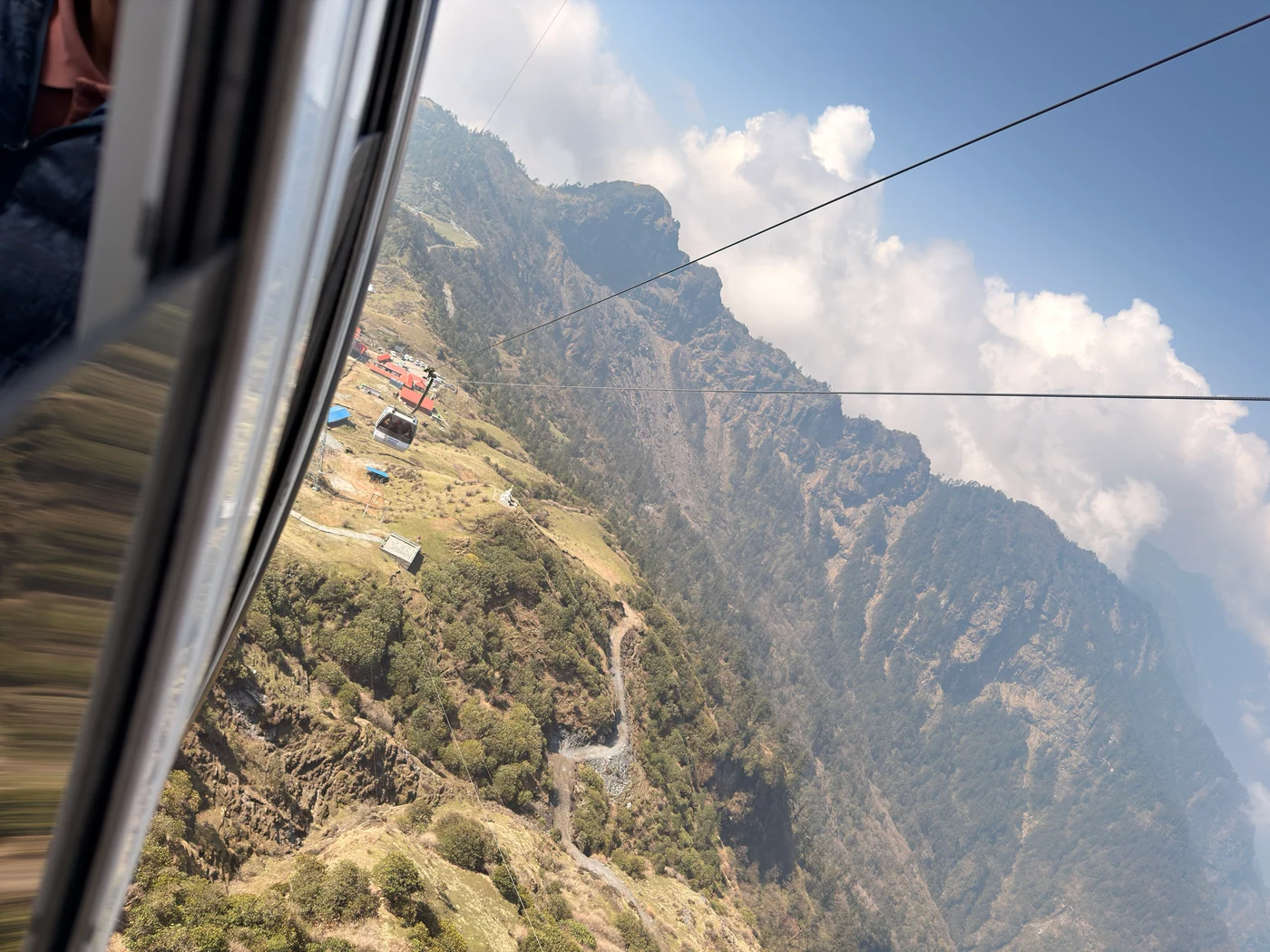 A mountain ridge and cable car seen through the window of another cable car